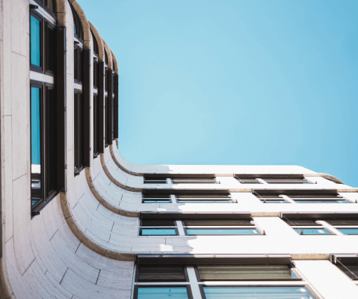 Contemporary architecture featuring a building with a curving, off-white stone facade and windows with dark frames, set against a clear blue sky.