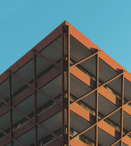 Low-angle view of a building with an exposed metal structure, geometric patterns, and an orange and gray color scheme.