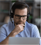 Man wearing a headset and glasses, looking at a laptop screen.